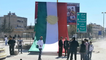 Protesters stand in front of a Kurdish flag in Qamishli (REUTERS/Handout)