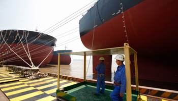 Workers stand in front of a 380,000 DWT class very large ore carrier (Reuters/Aly Song)