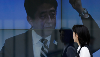 A woman walks past an electronic board displaying a photo of Prime Minister Shinzo Abe (Reuters/Toru Hanai)