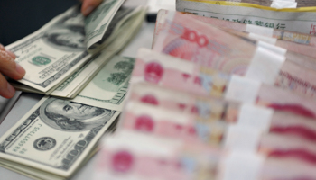 A bank clerk counts US dollar banknotes after counting Chinese 100 renminbi banknotes (Reuters/China Daily)