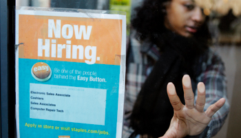 A woman opens a glass door with a "Now Hiring" sign on it in New York (Reuters/Lucas Jackson)