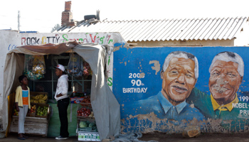 Youths stand outside a makeshift shop alongside a mural of Nelson Mandela in Soweto (Reuters/Siphiwe Sibeko)