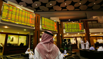 An investor looks up at screens displaying stock information (Reuters/Jumana El Heloueh)