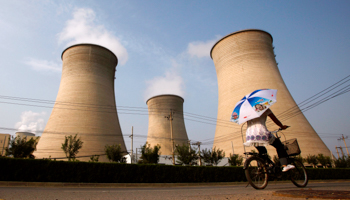 A woman holding an umbrella rides her bicycle along a road past a coal-burning power station in Beijing (Reuters/David Gray)