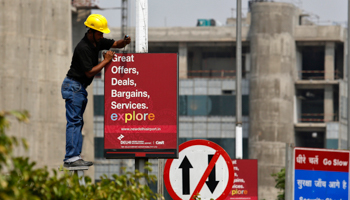 A worker removes a GMR Infrastructure board near to the airport in New Delhi (Reuters/Anindito Mukherjee)