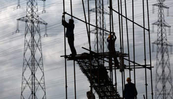 Construction workers stand on scaffolding in front of high voltage power lines in Shanghai (Reuters)