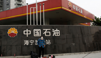 A garbage collector stands in front of a PetroChina company logo at its gas station in Shanghai (Reuters/Aly Song)