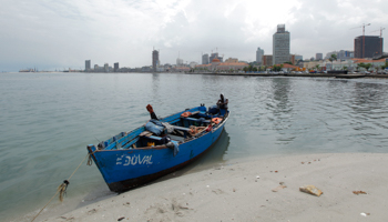 An Angolan fisherman sits by his boat against the backdrop of the capital Luanda (Reuters/Mike Hutchings)