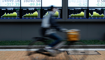 A man rides a bicycle past electronic boards outside a brokerage in Tokyo (Reuters/Yuya Shino)