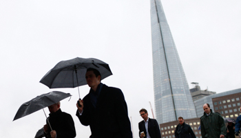 The Shard is seen as workers use umbrellas to shelter themselves from the rain while crossing London Bridge (Reuters/Eddie Keogh)