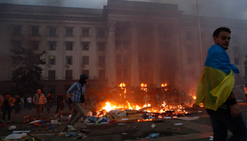 A man wrapped in a Ukrainian flag walks past a burning tent camp and a fire in the trade union building in Odessa (Reuters/Yevgeny Volokin)