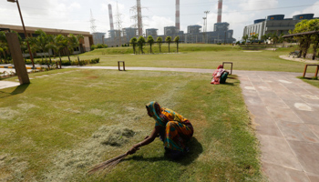 Workers remove dead grass against the backdrop of power plants of Adani Power at Mundra town in western India (Reuters/Amit Dave)