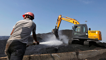 A worker sprays water over piles of coal as a bulldozer shifts coal in the western Indian state of Gujarat (Reuters/Amit Dave)