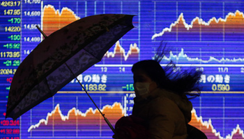 A pedestrian walks past a board showing the recent fluctuations of the Nikkei average in Tokyo (Reuters/Yuya Shino)