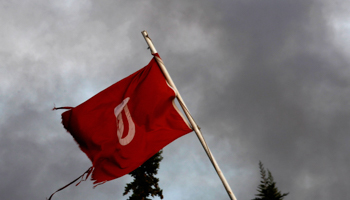 A Tunisian national flag is seen while smoke rises from a burnt government buildings in Sidi Bouzid (Reuters/Zohra Bensemra)