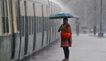 A woman holds an umbrella while waiting to board a train during a heavy rain shower at a railway station in Kolkata (Reuters/Rupak De Chowdhuri)