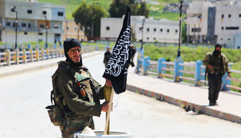 Al-Nusra Front fighter carries a shell near al-Nusra Front flag (REUTERS/Ammar Abdullah)