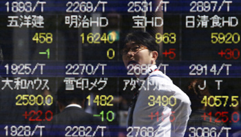 A pedestrian in Tokyo reflected in a board showing various stock prices (Reuters/Yuya Shino)