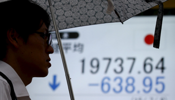 A man holding an umbrella walks past a brokerage in Tokyo (Reuters/Toru Hanai)