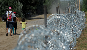A migrant family walks by a fence that is being built on the Hungarian Serbian border at Morahalom, Hungary (Reuters/Stringer)