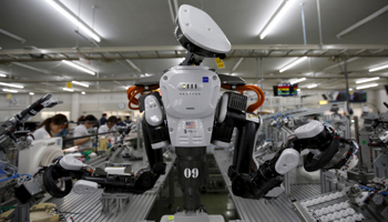 A humanoid robot works side by side with employees in the assembly line at a manufacturer of automatic change dispensers, in Kazo, Japan (Reuters/Issei Kato)