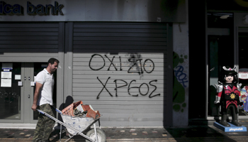 Graffiti on a closed Attica Bank branch reads, "No to the debt" as a worker pushing a cart walks by, Athens (Reuters/Alkis Konstantinidis/Files)
