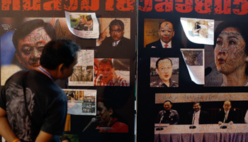 An anti-government protester looks at defaced pictures of former Prime Ministers Yingluck Shinawatra and Thaksin Shinawatra (Reuters/Athit Perawongmetha)