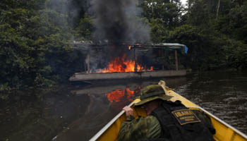 A Brazilian environmental agent burns an illegal gold dredge at the Uraricoera River (Reuters/Bruno Kelly)