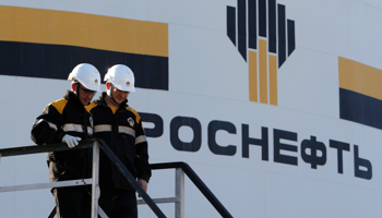 Workers stand next to a logo of Russia's Rosneft oil company (Reuters/Sergei Karpukhin)