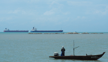 A dry bulk ship passes a fisherman off the coast of Johor, Malaysia (Reuters/Henning Gloystein)
