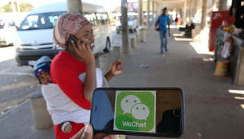 A WeChat logo is displayed on a mobile phone as a woman walks past a Johannesburg taxi rank (Reuters/Siphiwe Sibeko)