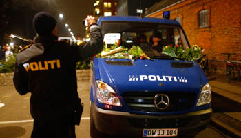 A policeman takes photos of a police vehicle covered with flowers after a memorial service held for those killed on Saturday by a 22-year-old gunman, in Copenhagen February 16, 2015 (Reuters/Hannibal Hanschke)