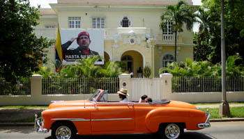 Tourists ride in a vintage car as it passes in front of a picture of Venezuela's late president Hugo Chavez hung at the Venezuelan embassy in Havana, Cuba (Reuters/Alexandre Meneghini)