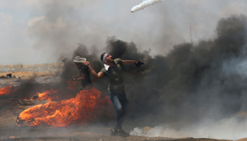 A Palestinian demonstrator uses a racket to return a tear gas canister fired by Israeli troops, Southern Gaza Strip, May 11 (Reuters/Ibraheem Abu Mustafa)