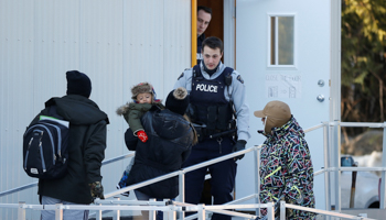 Royal Canadian Mounted Police officers look on as people enter a trailer after crossing the US-Canada border into Canada in Lacolle, Quebec, Canada (Reuters/Chris Wattie)