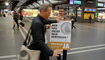 A member of the sovereign money initiative campaigning in Zurich, Switzerland in May 2018. The poster reads, "Who should produce our money? Sovereign money yes - Swiss francs from National Bank only". (Reuters/Arnd Wiegmann)