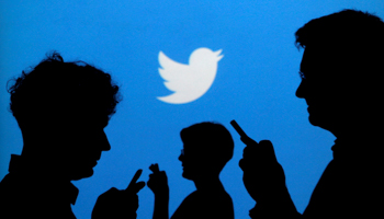People holding mobile phones are silhouetted against a backdrop projected with the Twitter logo (Reuters/Kacper Pempel)