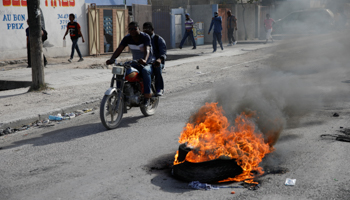 Two men ride a motorbike past a burning barricade along a street in Port-au-Prince, Haiti, June 18 (Reuters/Andres Martinez Casares)