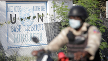 A Haitian National Police (PNH) officer drives a motorbike past a sign of the Logistic Base of the United Nations Mission for Justice Support in Haiti, Port-au-Prince, October 14 (Reuters/Andres Martinez Casares)