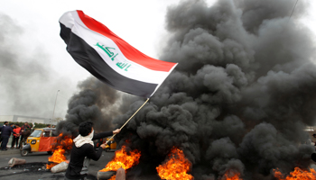 A demonstrator carries an Iraqi flag as he walks near burning tyres blocking a road during ongoing anti-government protests, in Baghdad, Iraq, January 19 (Reuters/Khalid al-Mousily)