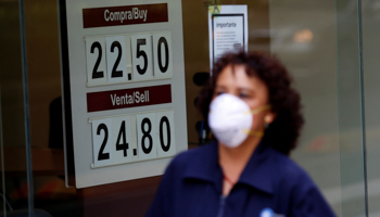 A woman wearing a mask walks past a board displaying the peso-dollar exchange rate at a currency exchange shop in Mexico City (Reuters/Gustavo Graf)