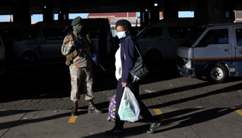 A commuter wearing a protective mask walks past a member of the South African National Defence Force (SANDF) in Soweto, June 1 (Reuters/Siphiwe Sibeko)