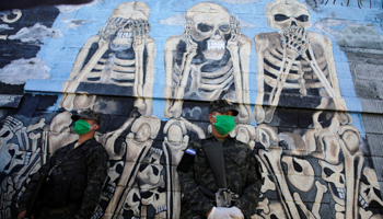 Honduran army personnel stand in front of a gang mural during the COVID-19 outbreak, Tegucigalpa, Honduras, March 27 (Reuters/Jorge Cabrera)