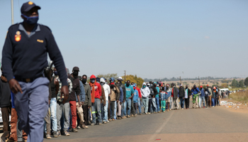 A police officer walks past people queuing for food aid, Sunderland Ridge, South Africa, May 14 (Reuters/Siphiwe Sibeko)