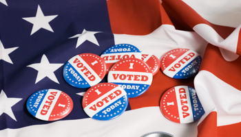 US 'I voted' buttons atop the US flag (grejak / Shutterstock)