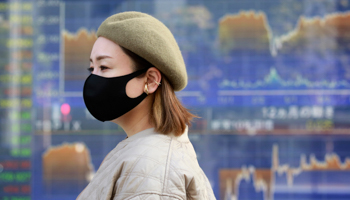 A woman walks by an electronic stock board of a securities firm in Tokyo (Koji Sasahara/AP/Shutterstock)
