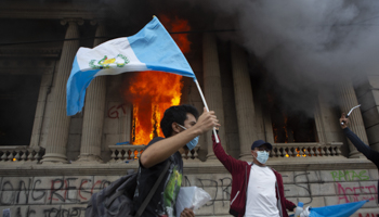 A protester waves the national flag in front of Guatemala’s burning Congress building, Guatemala City, November 21 (Oliver De Ros/AP/Shutterstock)