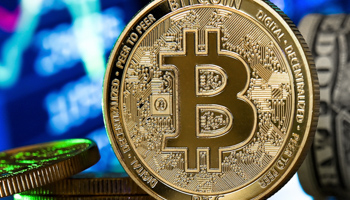 A bitcoin reflects in front of a monitor showing a stock barometer in Duesseldorf, Germany, January 2021 (SASCHA STEINBACH/EPA-EFE/Shutterstock)