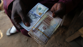 A money changer holds a 100-dollar-note and naira notes in a street in Sapon district in Abeokuta, December 11, 2020 (Akintunde Akinleye/EPA-EFE/Shutterstock)