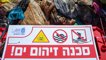 Warning sign and bags of tar on a Israeli beach after an oil spill, February 2021 (Ariel Schalit/AP/Shutterstock)